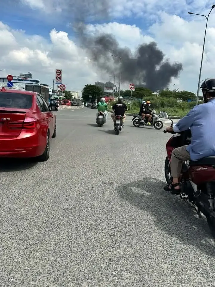 Cột khói đen bốc cao phía xa nhìn từ một tuyến đường có xe máy và ô tô đang chạy